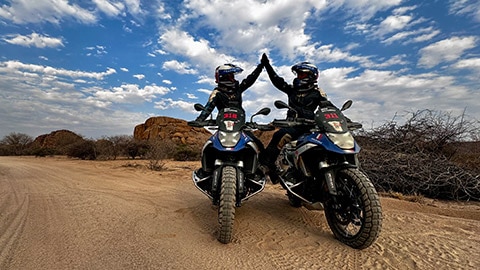 Fransız kadın takımından iki sürücü R 1300 GS Competition Motosikletleri üzerinde yan yana otururken birbirlerini kutluyor.