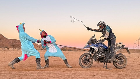 Tek boynuzlu at kostümü içinde Alman takımından iki sürücü bir R 1300 GS’e bağlı çekme halatını çekiyor. Üçüncü sürücü kırbacıyla motosikleti üzerinde oturuyor.