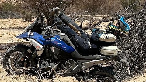 Japon kadın takımından bir sürücü R 1300 GS motosikleti üzerinde yatıyor. Bacaklarını gidonlara doğru uzatırken, başı ve omuzları motosikletin arkasından taşıyor.